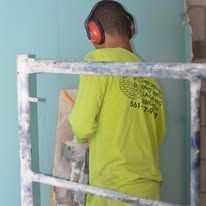 Worker in neon shirt and ear protection painting a wall behind a scaffold.