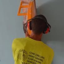 Worker in yellow shirt and headphones using an orange drill on a wall