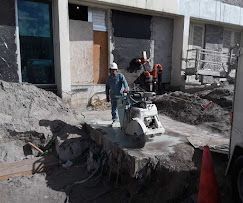 Construction worker using a concrete saw near a large trench outside a building entrance