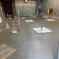 Indoor concrete floor under construction with several leveling posts and a staircase in the background