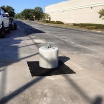 Metal trash can on a black mat in an empty sunny parking lot beside a beige building
