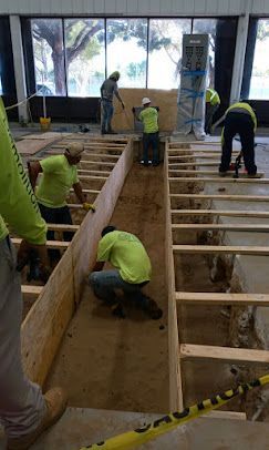 Workers in neon vests build a wooden ramp inside a large room with caution tape at the edges