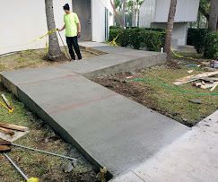 Concrete ramp leading to a building entrance, with a worker holding a hose nearby.