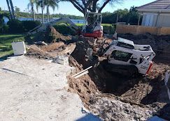Collapsed driveway with an excavator and a tipped white vehicle in a large sinkhole near a house.