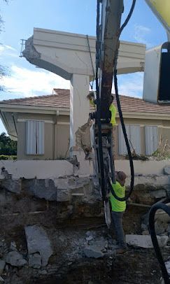 Utility worker in neon vest repairing a damaged building wall beside a utility pole.