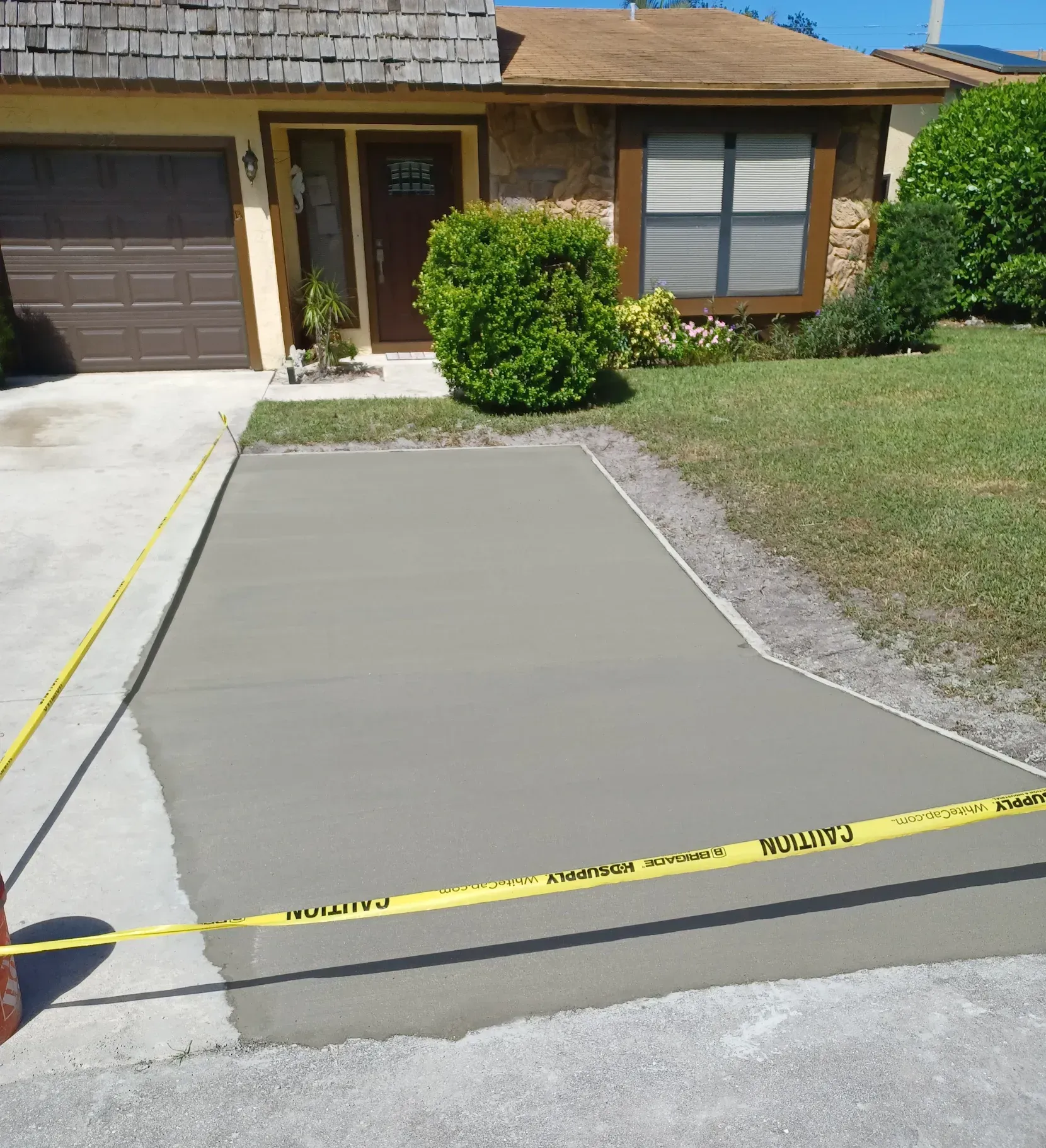 Freshly poured concrete driveway or walkway in front of a house, blocked off with yellow caution tape.