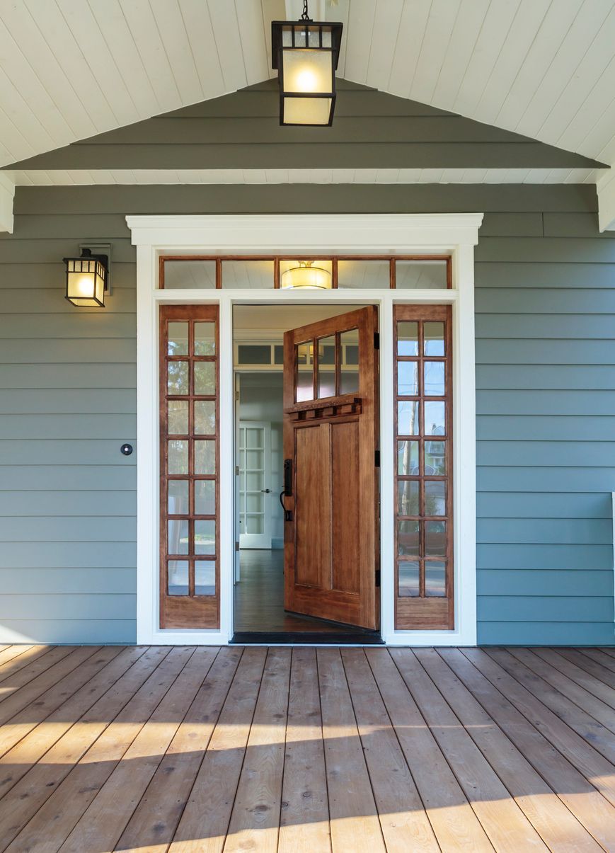 Wooden doorway with sidelights on a porch, door open, with light fixtures, blue siding.