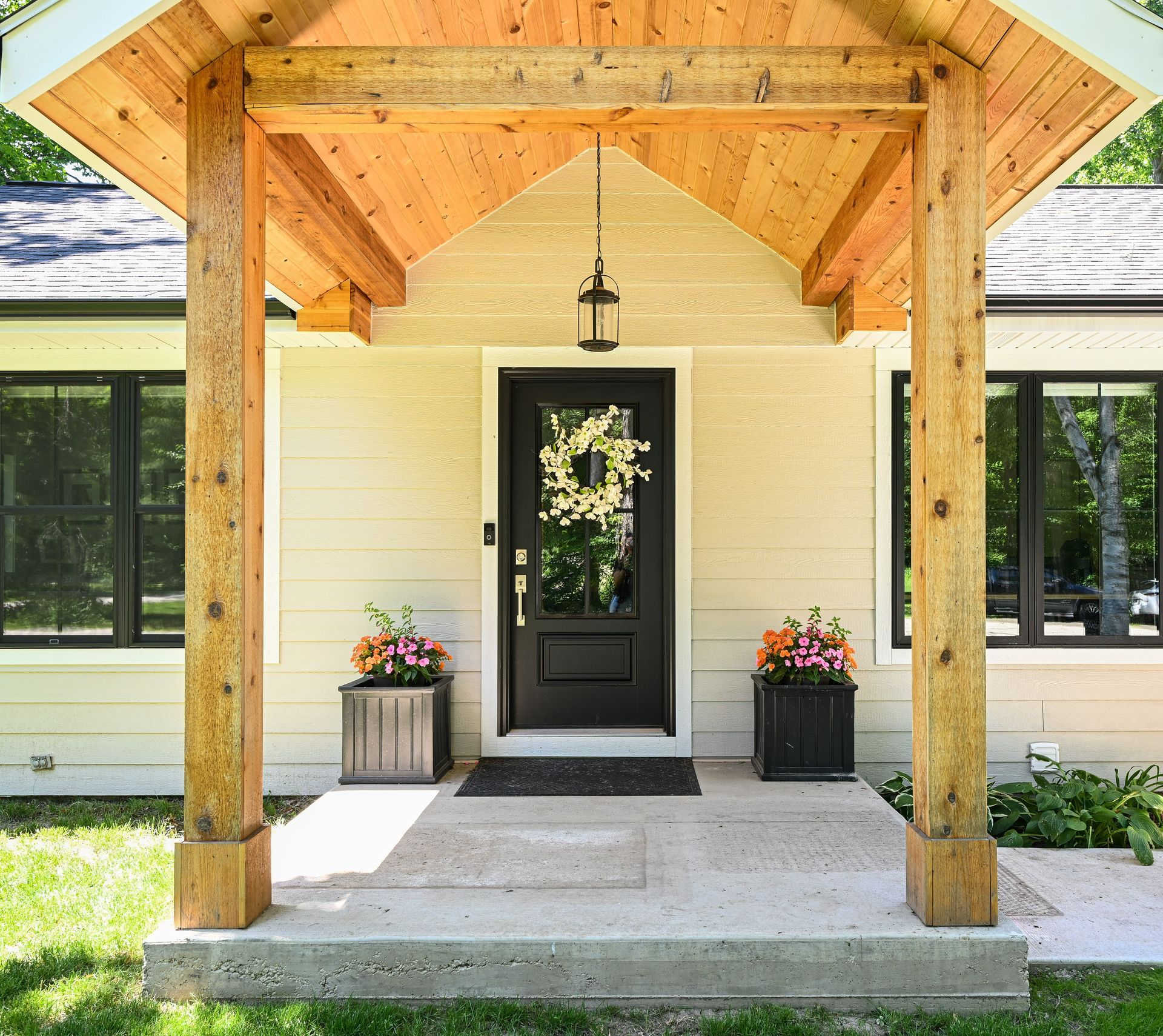 Beige house entrance with black door, wooden porch and planter boxes.