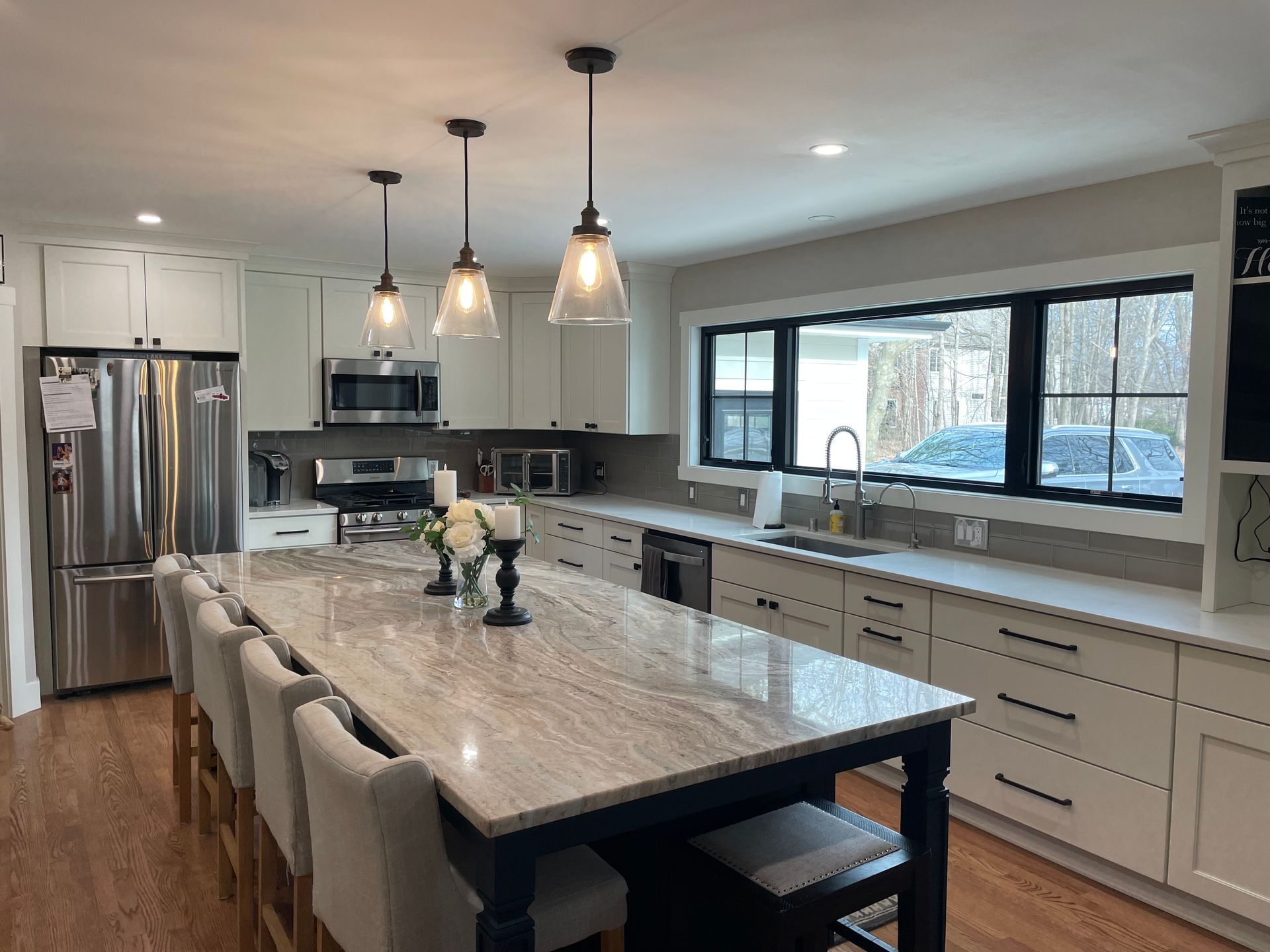 Modern kitchen with island, white cabinets, stainless steel appliances, and large windows.