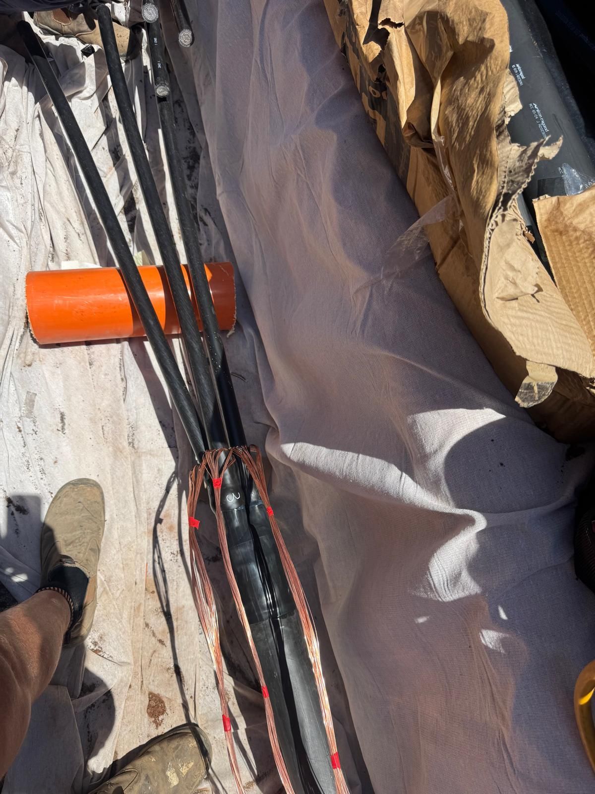 Orange pipe and bundled black cables on a concrete surface beside cardboard and a tarp