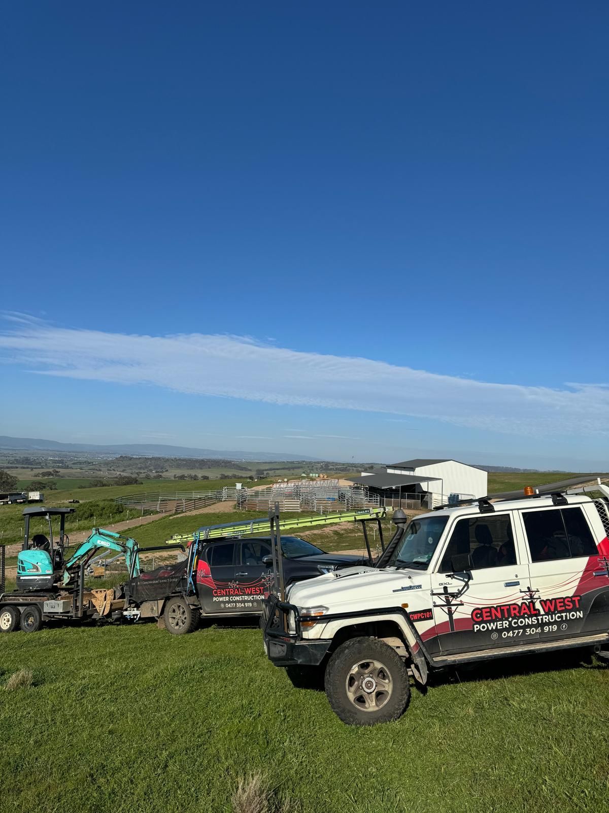 White SUV and off-road vehicles on a grassy hill under a clear blue sky, overlooking a rural landscape