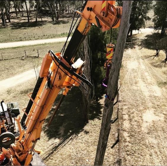 Crane Lifting a Utility Pole in a Rural Setting. Yellow Crane Arm, Dirt Road — Central West Power Construction in Orange, NSW