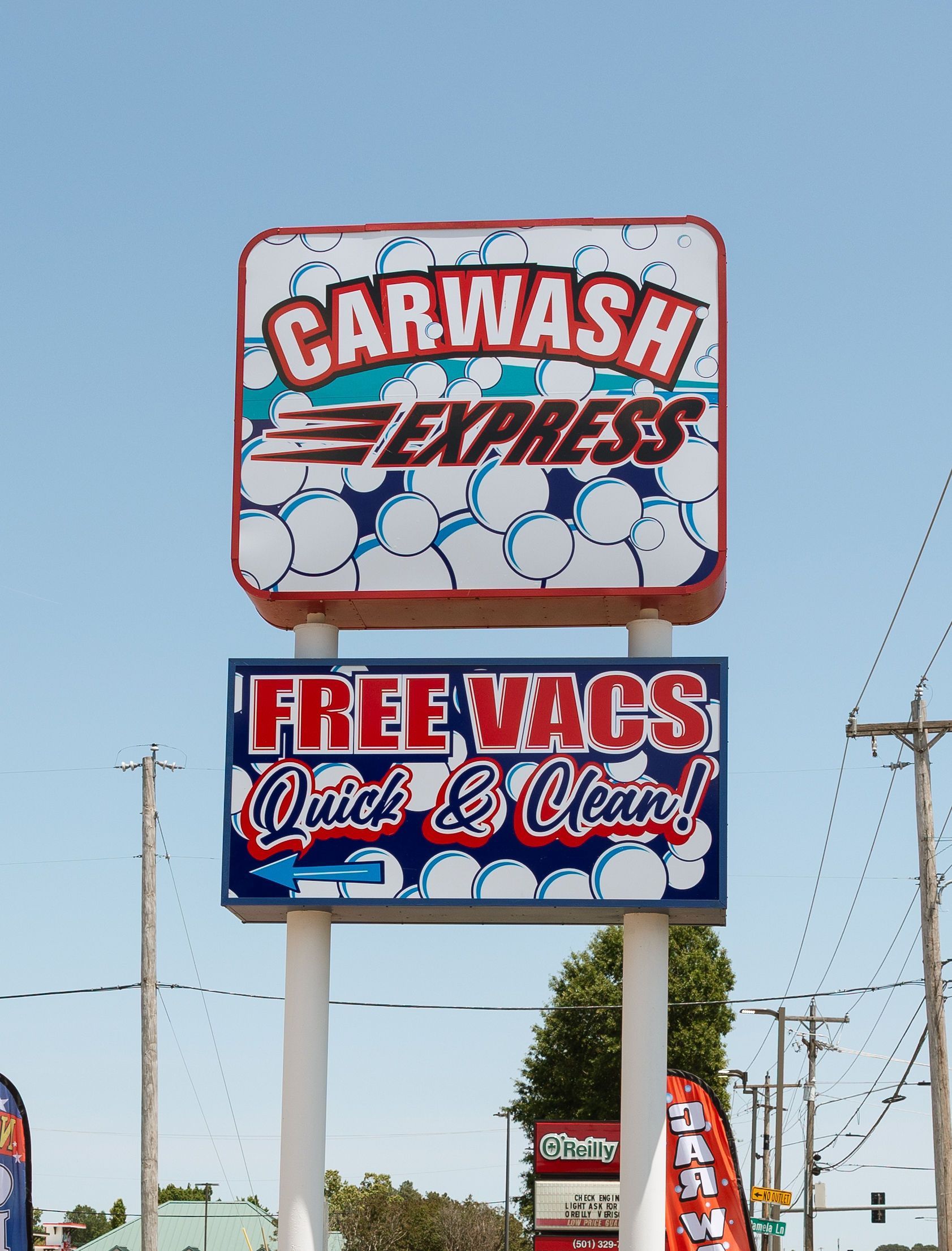 Two stacked roadside signs for Car Wash Express and Free Vacs against a blue sky