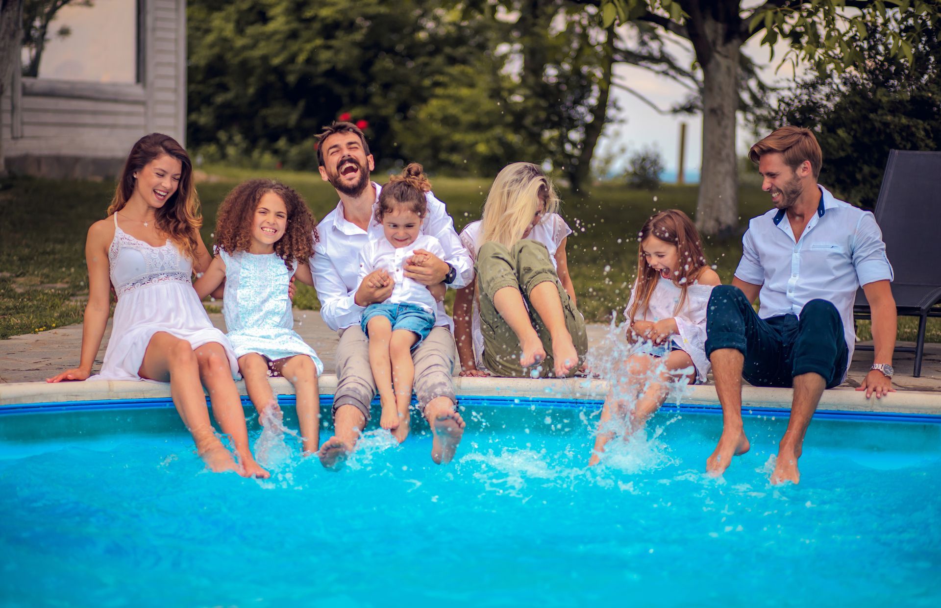 A large family is sitting on the edge of a swimming pool, splashing each other.