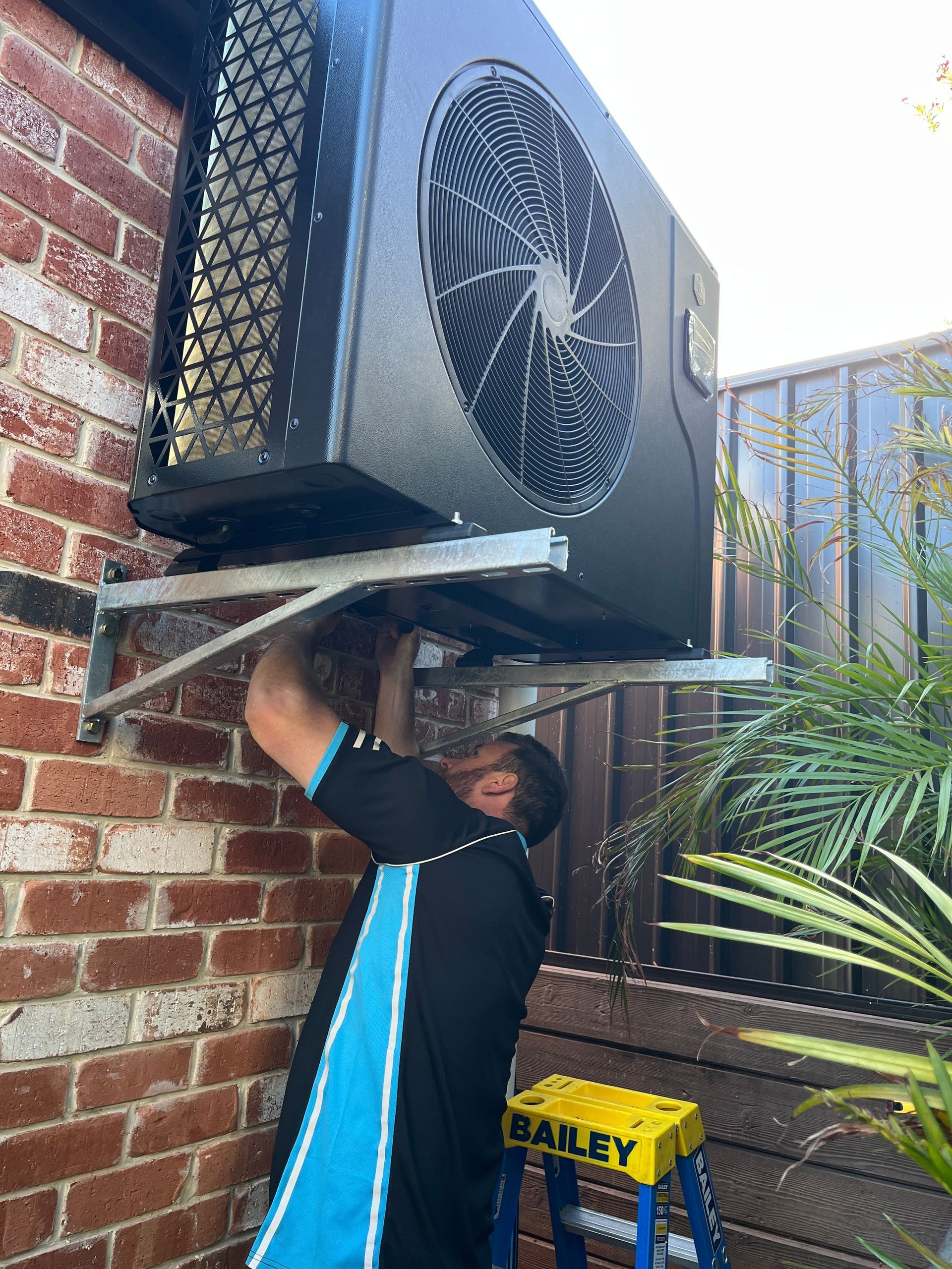 A technician wearing a black and blue uniform is performing heat pump service