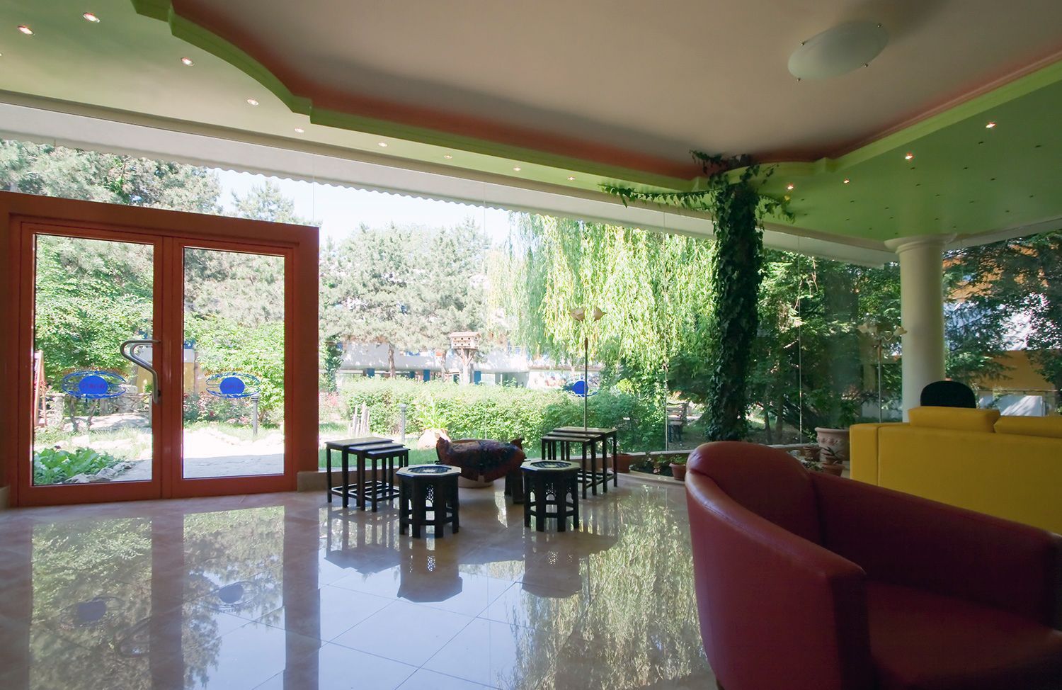 Bright living room with glossy floor, red chairs, green walls, and open glass doors to a garden.