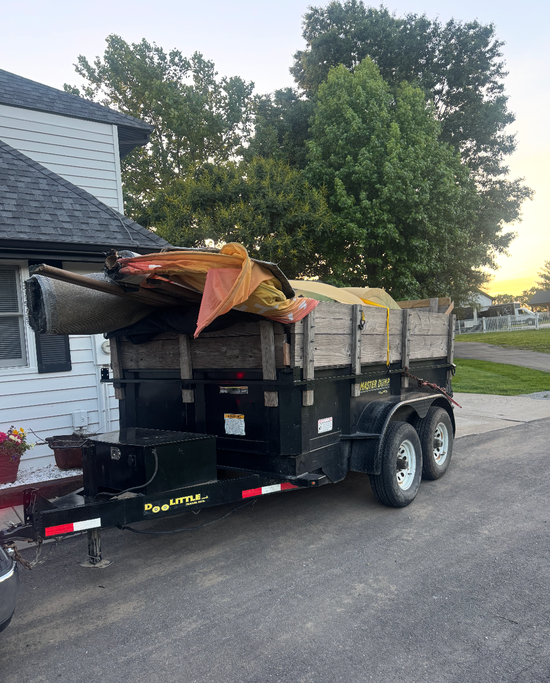 Two workers in uniform remove old carpet from a residential home, loading materials into a truck parked outside.