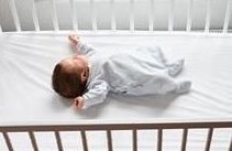 A baby is on its back and sleeping in a crib.