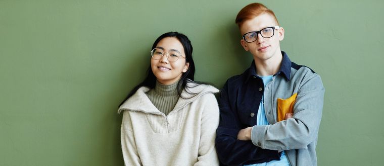 A man and a woman are standing next to each other in front of a green wall.