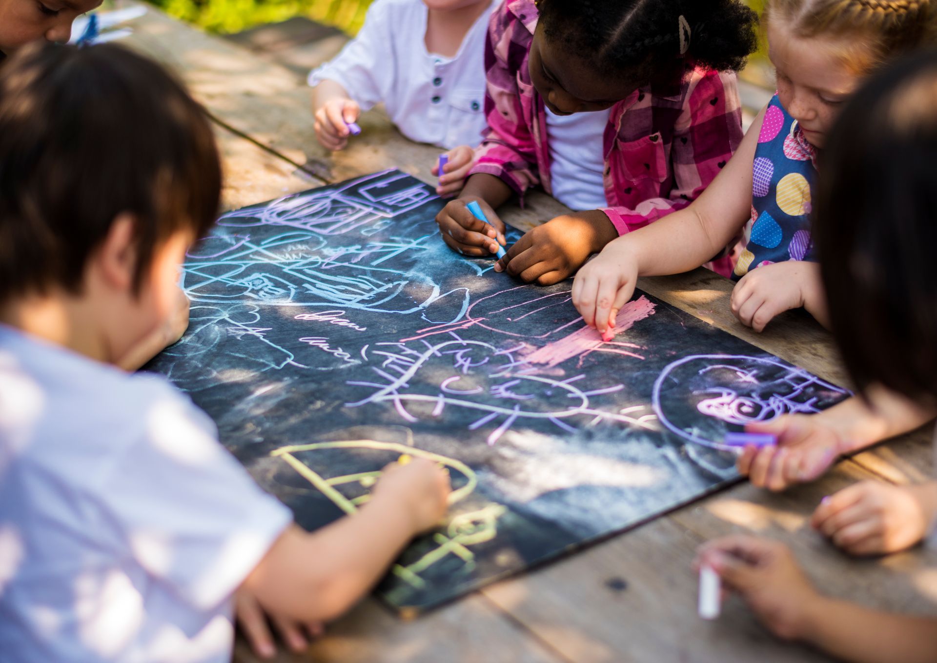 Children drawing with chalk on a blackboard on a table.