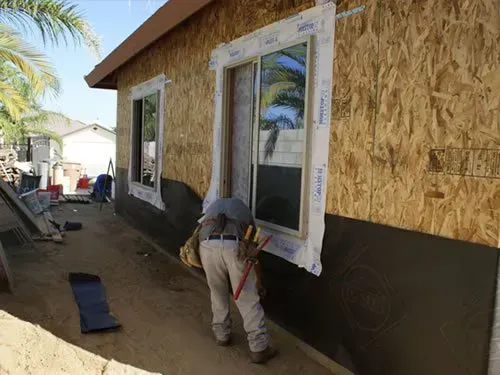 A man is installing a window on the side of a house.