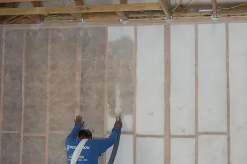 A man is blowing insulation into a wall with a vacuum.