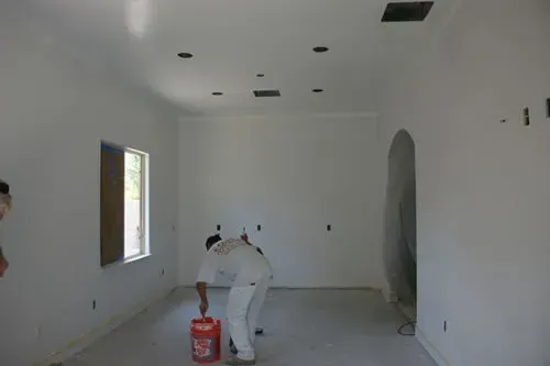 A man is kneeling down in a room with a bucket of paint.