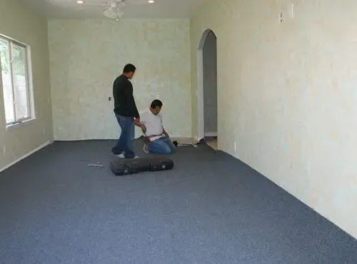 Two men are installing a carpet in an empty room.