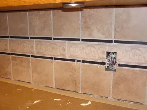 A close up of a tiled wall with a electrical outlet.
