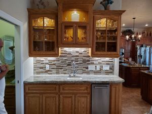 A man is standing in a kitchen with wooden cabinets and a sink.