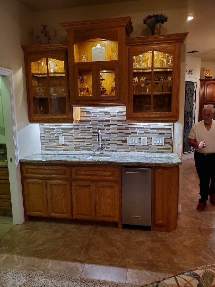 A man is standing in a kitchen with a sink and a dishwasher.