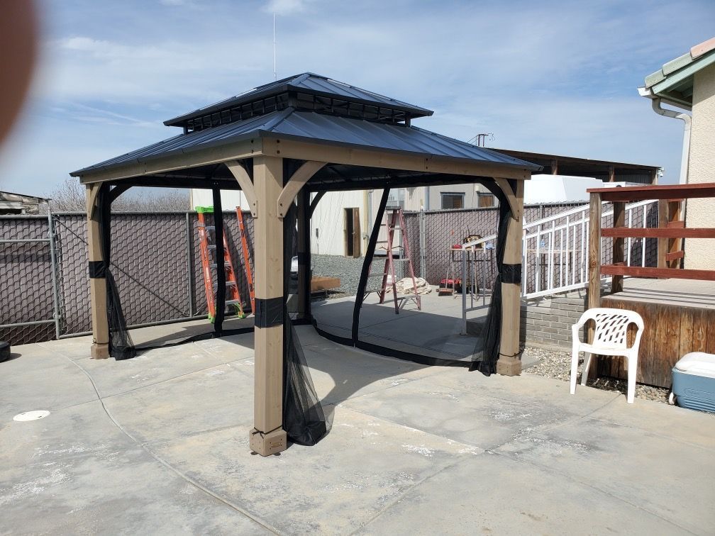 A gazebo is sitting on top of a concrete patio next to a chair.