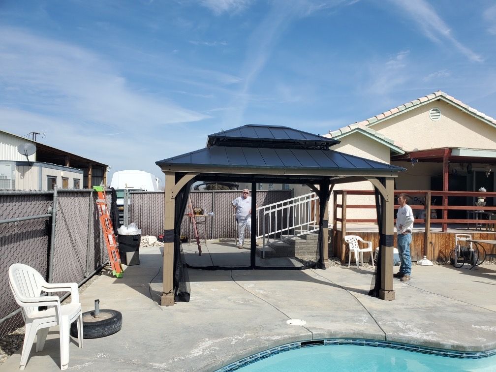 A man is standing in front of a gazebo next to a pool.
