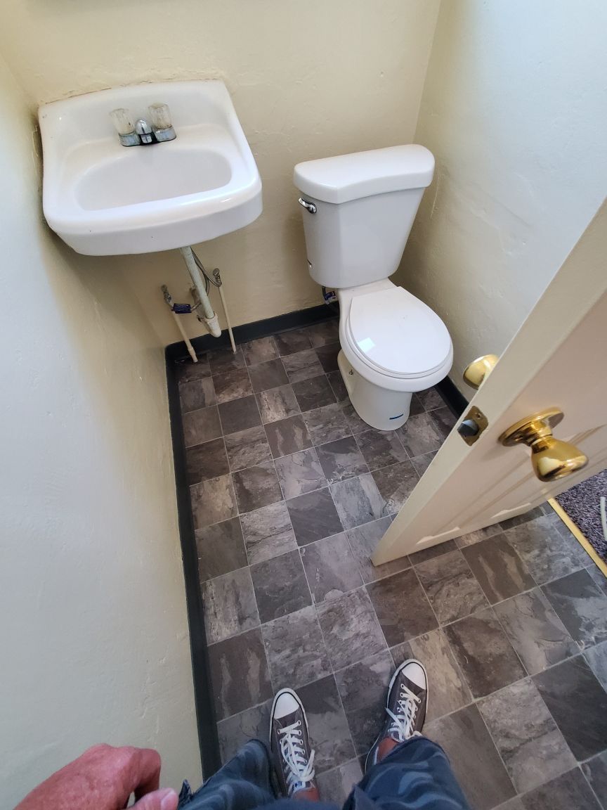 A person is standing in a bathroom with a sink and toilet.