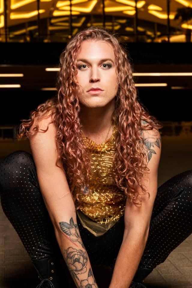 A woman with long red hair and tattoos is kneeling down on the floor.
