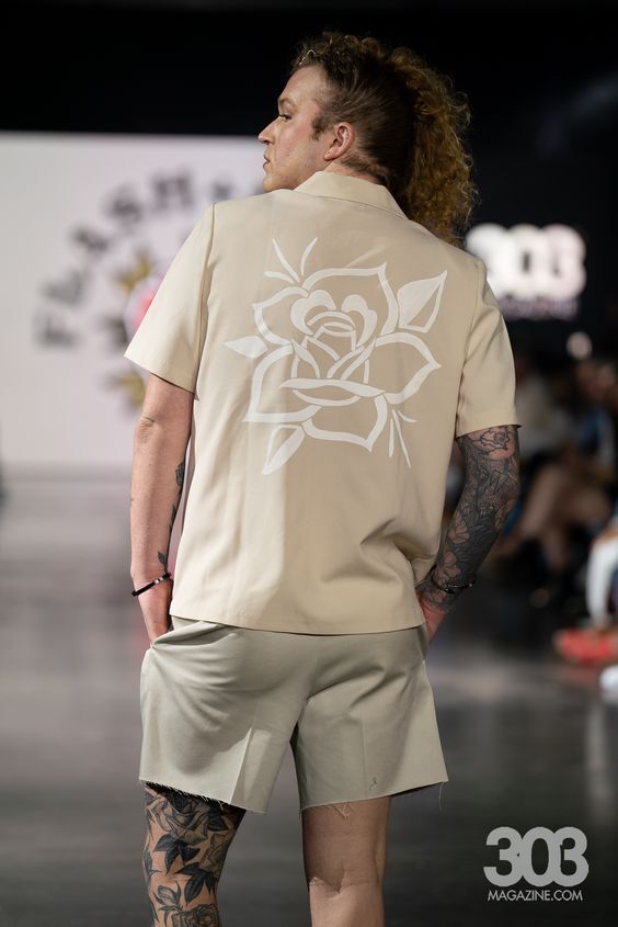 A man is walking down a runway for a fashion show wearing a shirt with a white rose on the back.