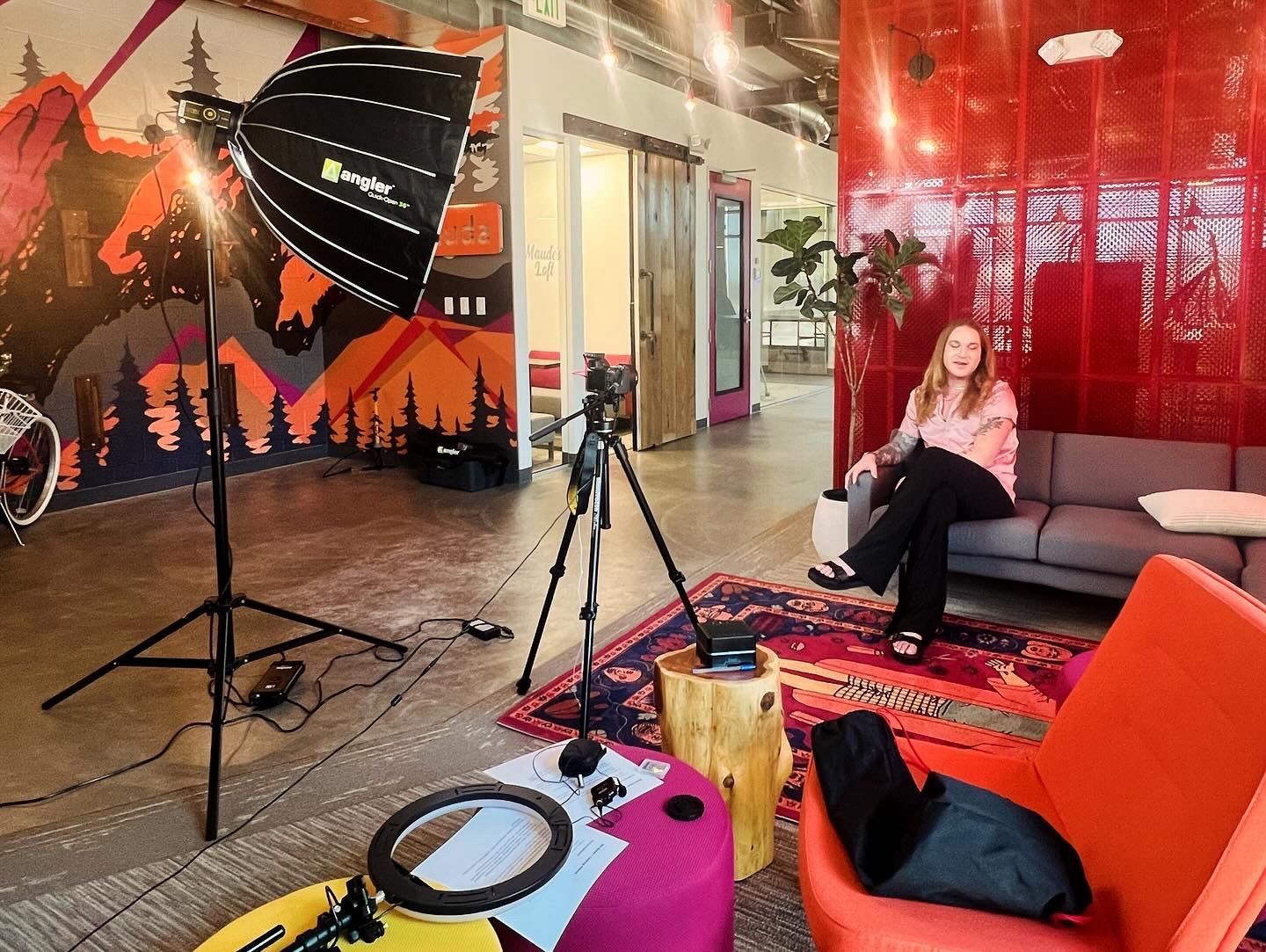 A woman is sitting on a couch in a living room with a camera on a tripod.
