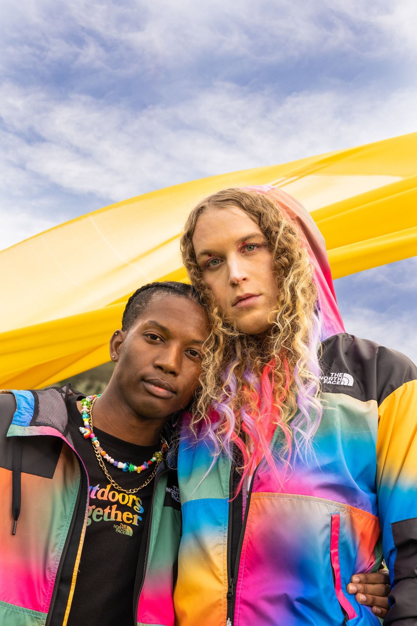 A man and a woman are standing next to each other in front of a yellow flag for a NorthFace photo shoot.