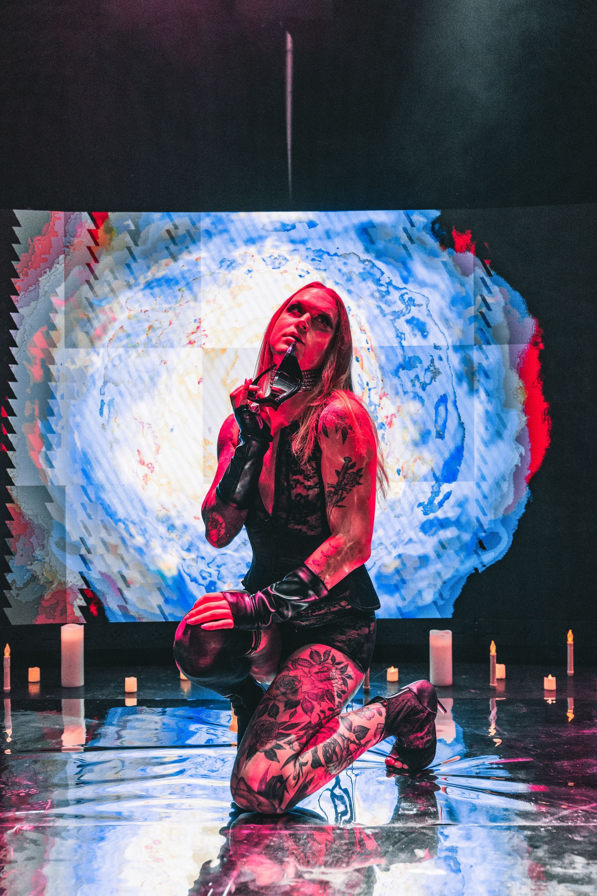A woman is kneeling down and singing into a microphone on a stage for a photoshoot.