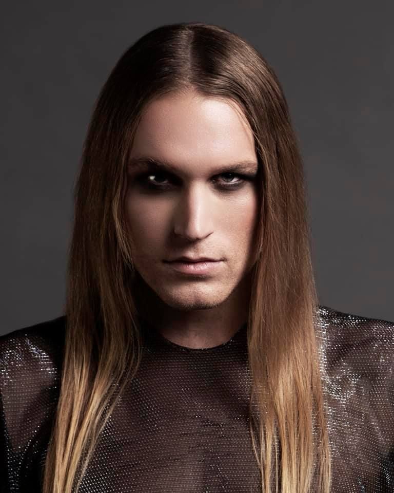 A man with long hair is wearing a black shirt for a photoshoot.