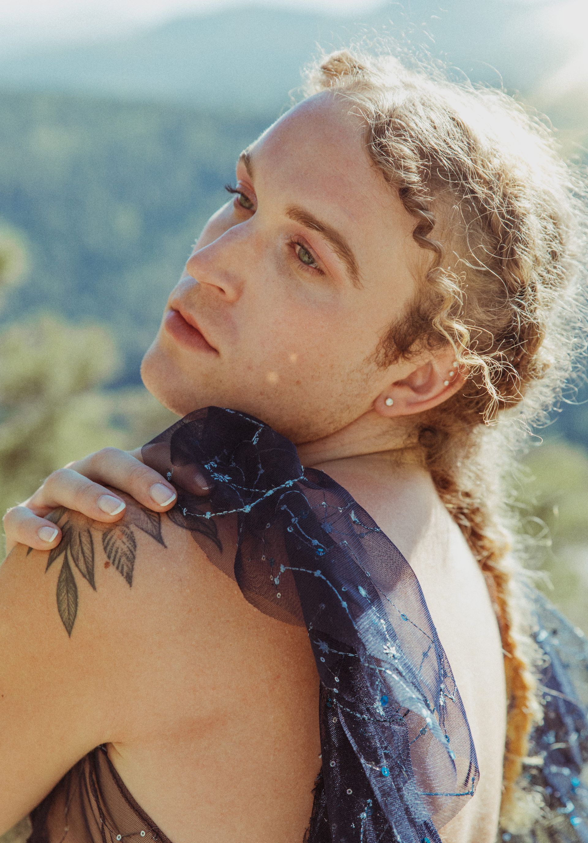A man with a tattoo on his shoulder is standing in front of a mountain.