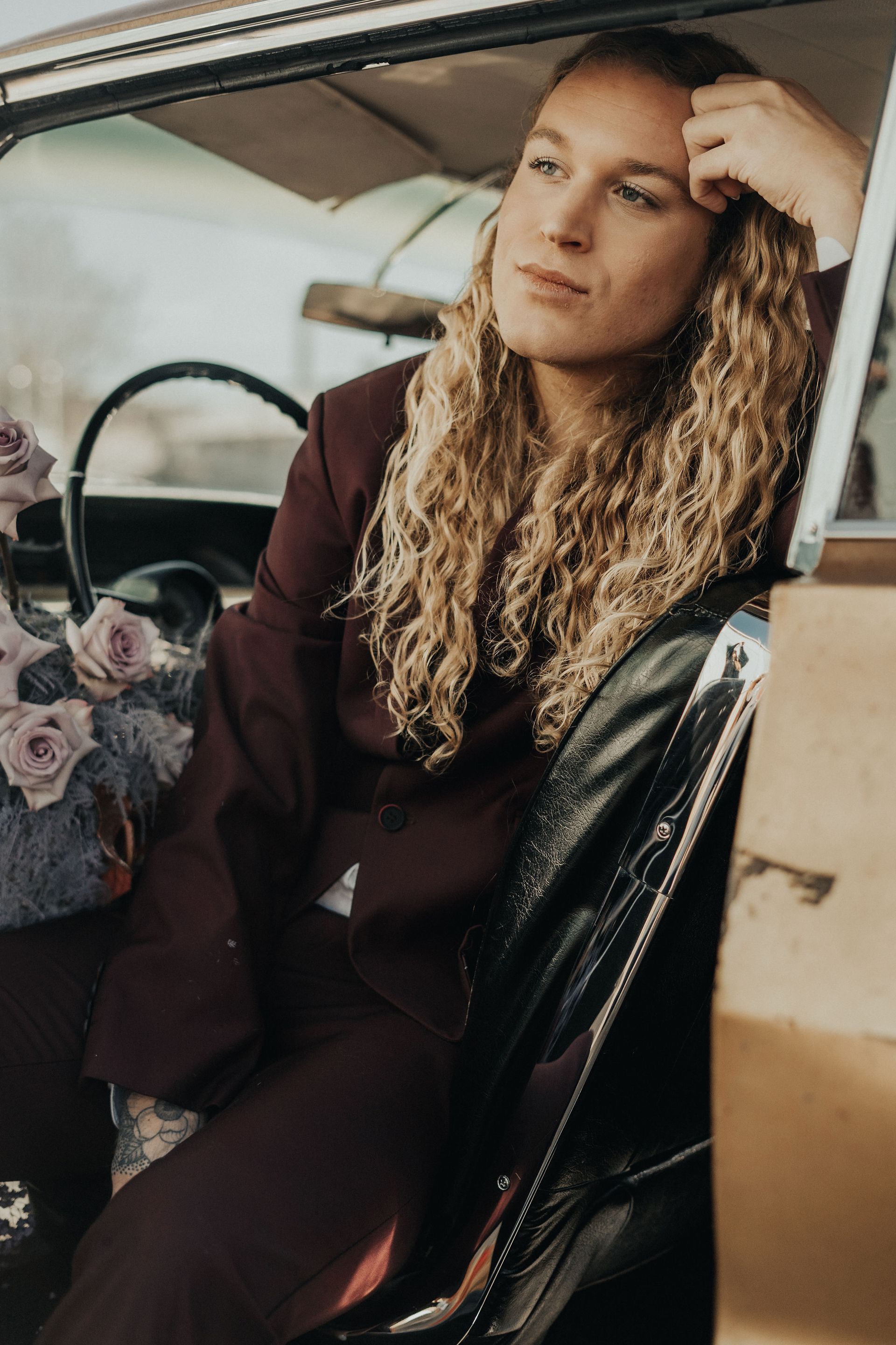 A model is sitting in the back seat of a car, looking out the window for a photo shoot.