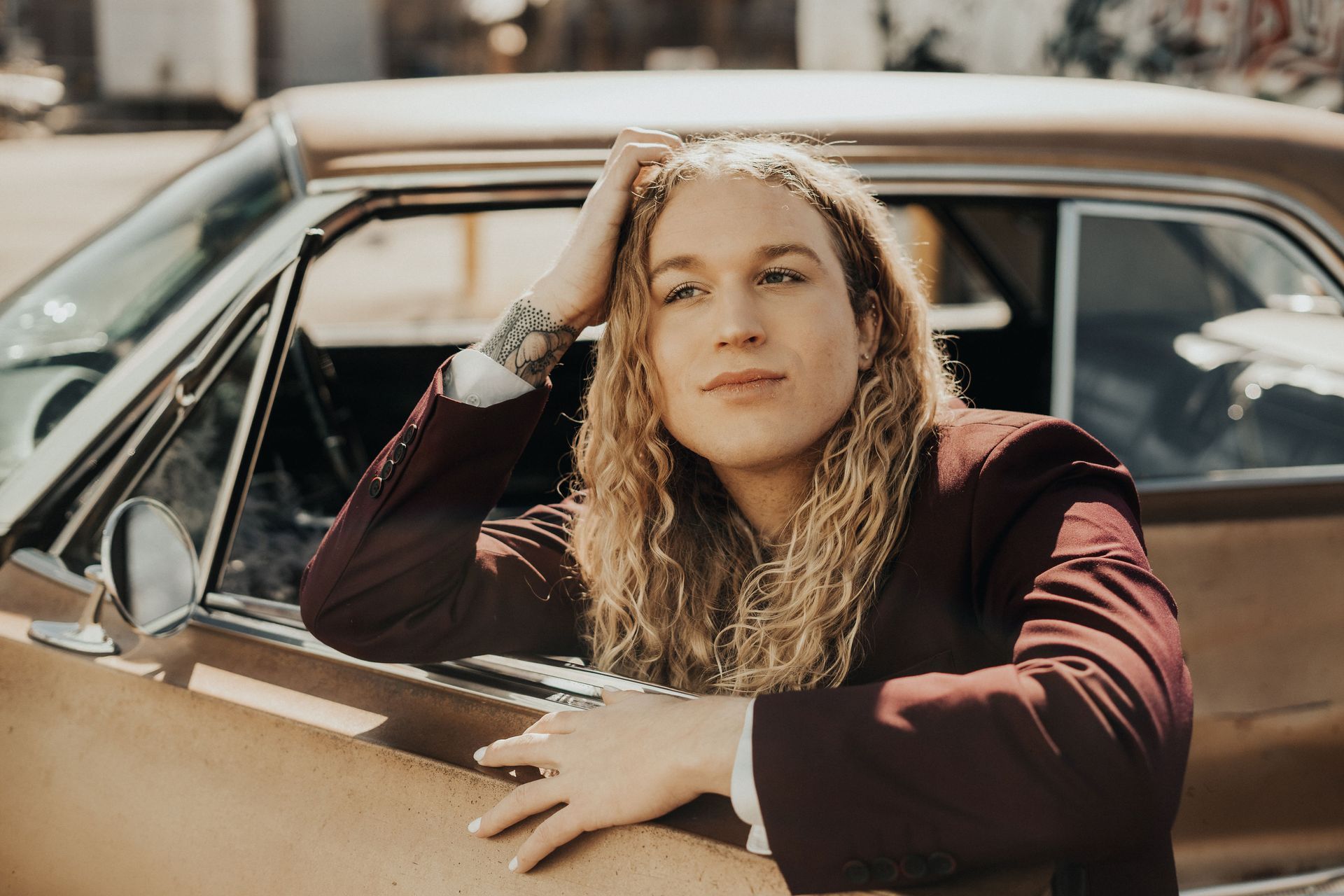 Scotty wearing a maroon suit posing in a car with flowers, modeling for a photoshoot