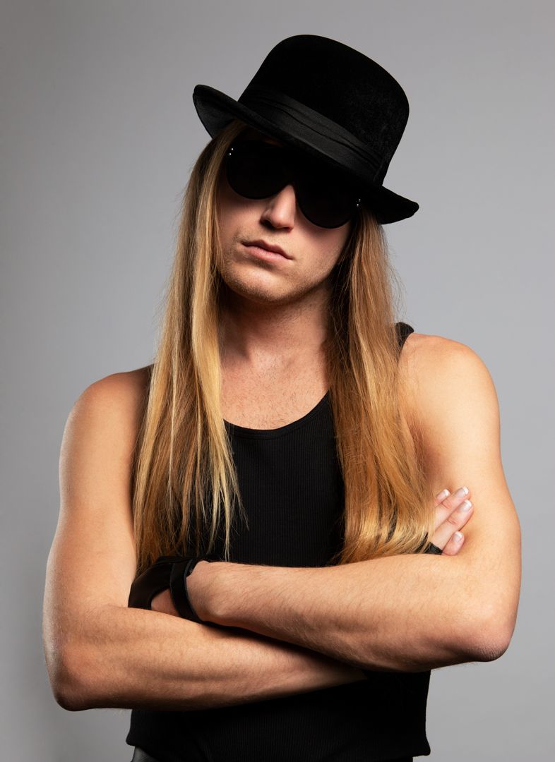 A man with long hair wearing a hat and sunglasses for a photoshoot.