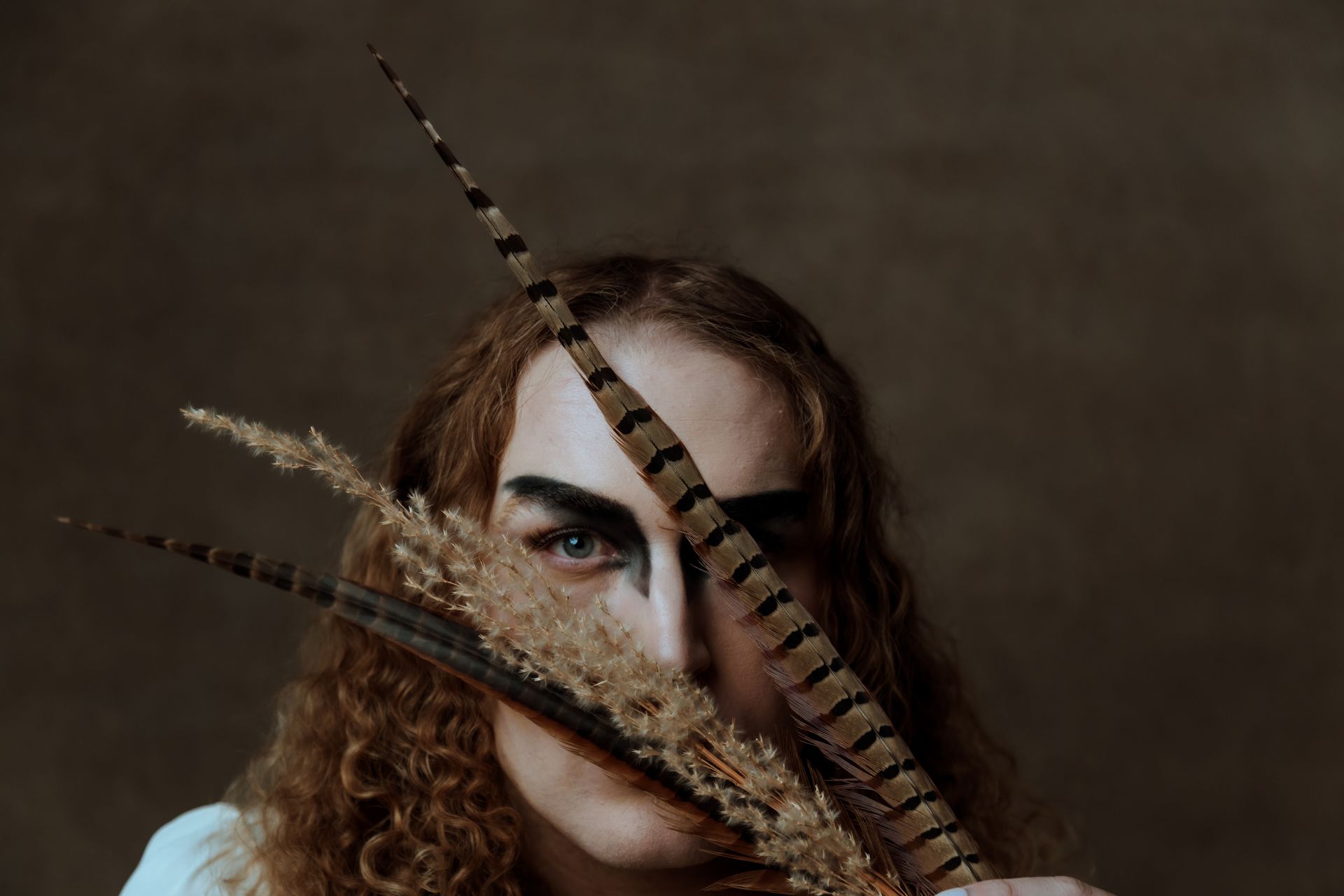 A woman is holding a feather in front of her face for a fashion photo shoot.