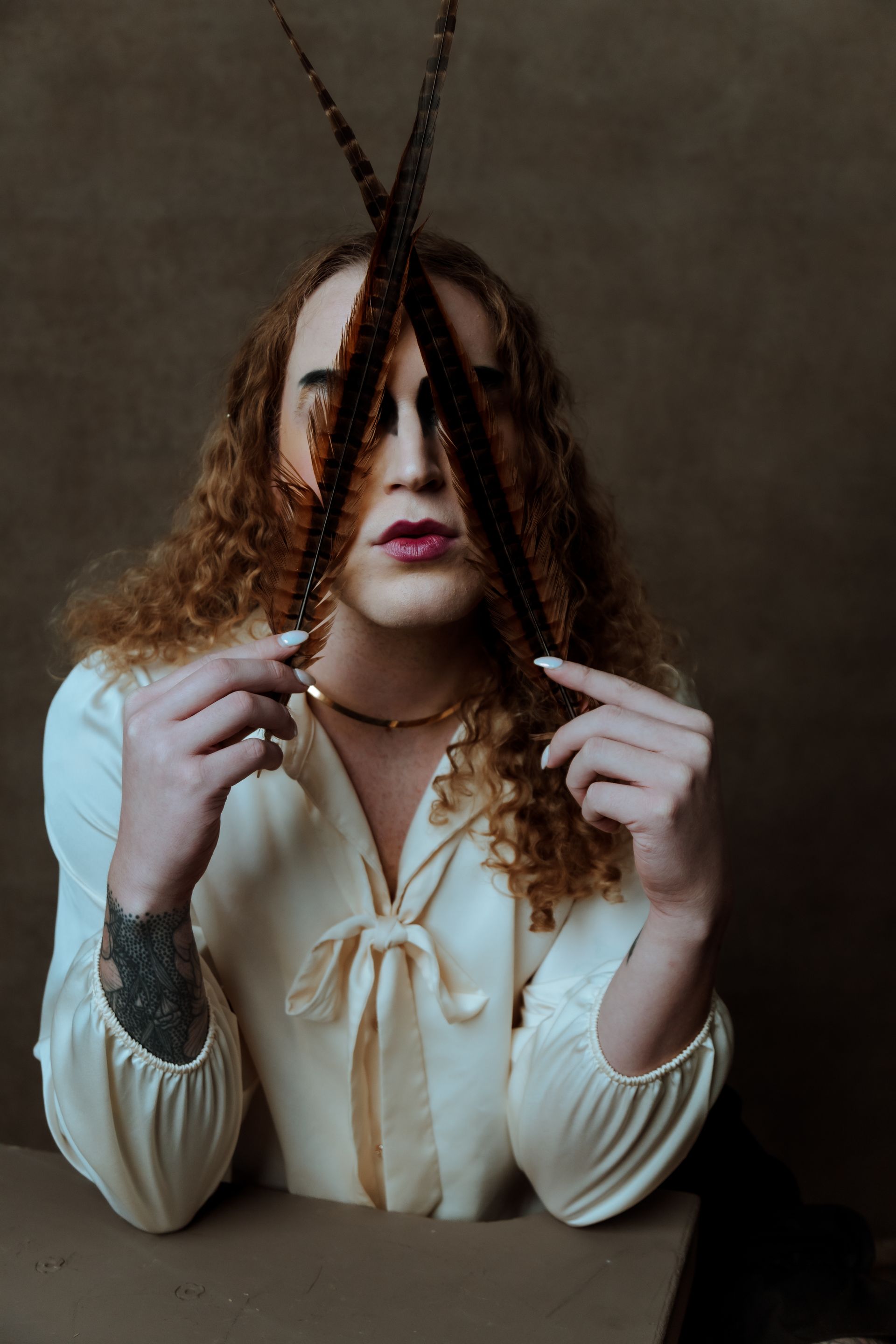 A woman is holding feathers in front of her face for a fashion photo shoot.