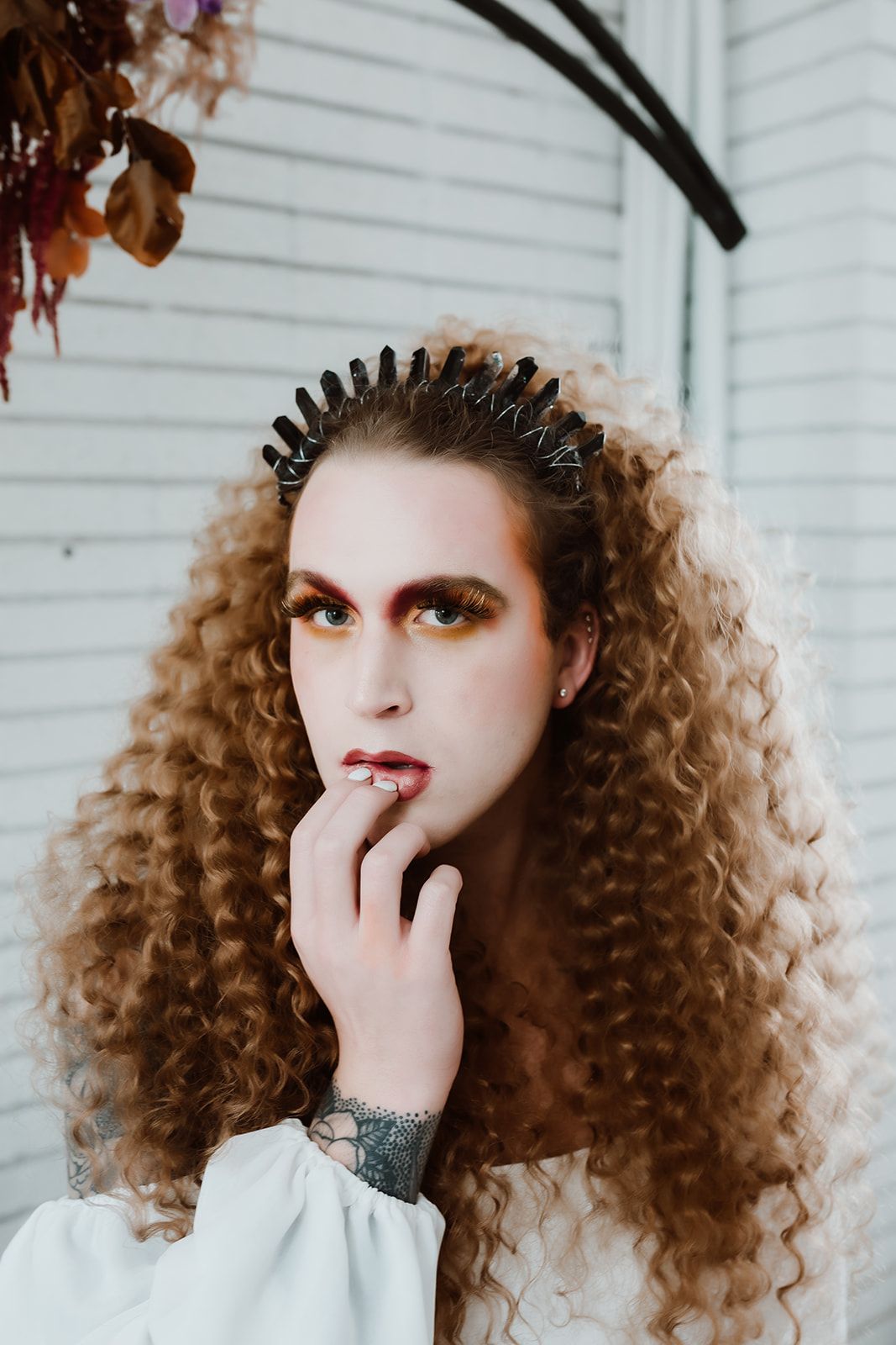 A man with curly hair is wearing a crown on his head for a photo shoot.