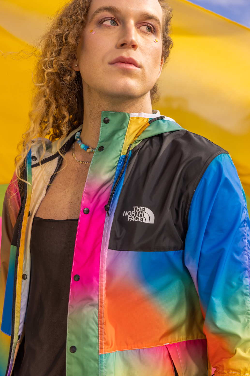 A man wearing a colorful jacket is standing in front of a rainbow flag for a NorthFace photo shoot.
