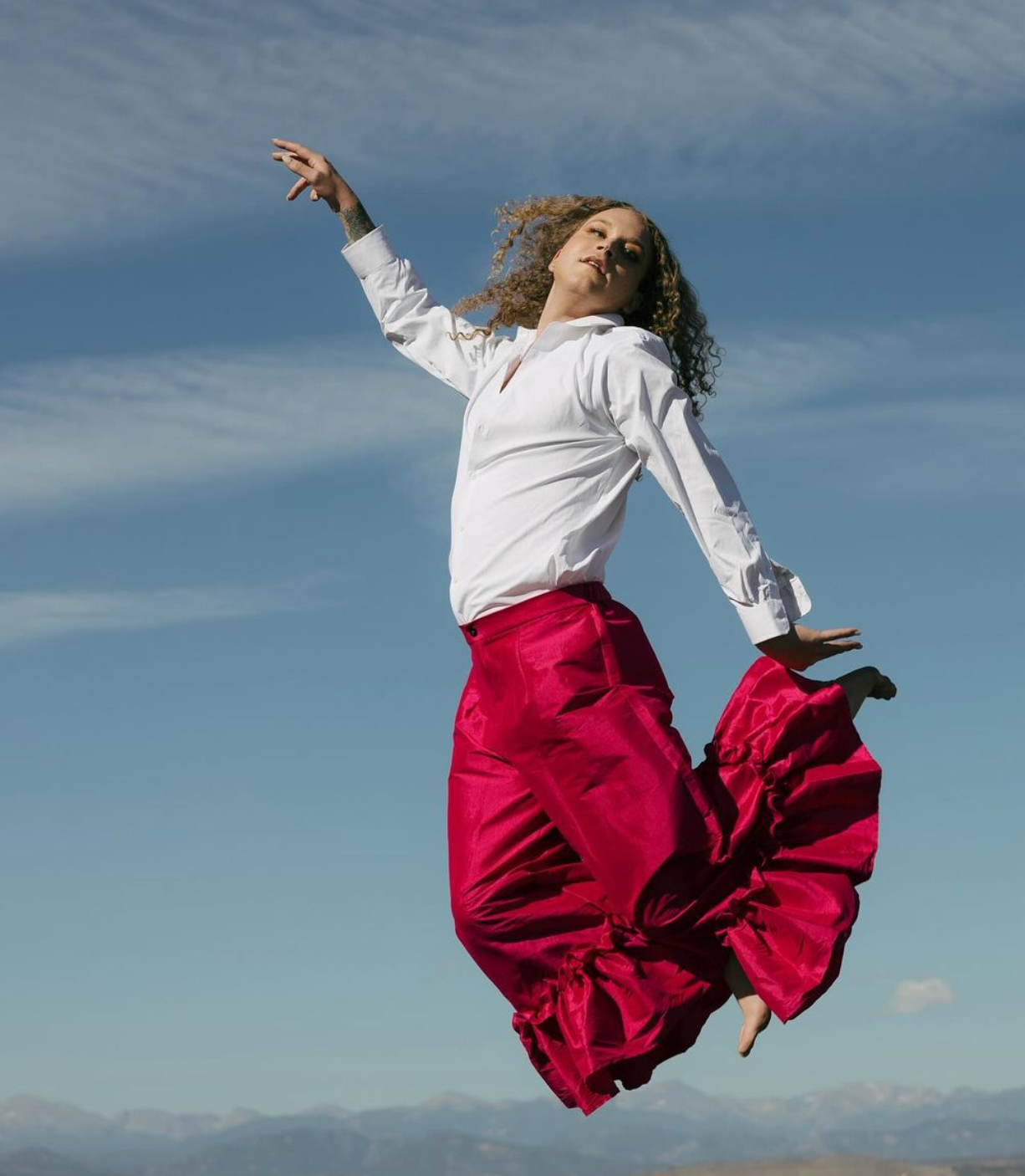 A man in a white shirt and red skirt is jumping in the air for a photo shoot.