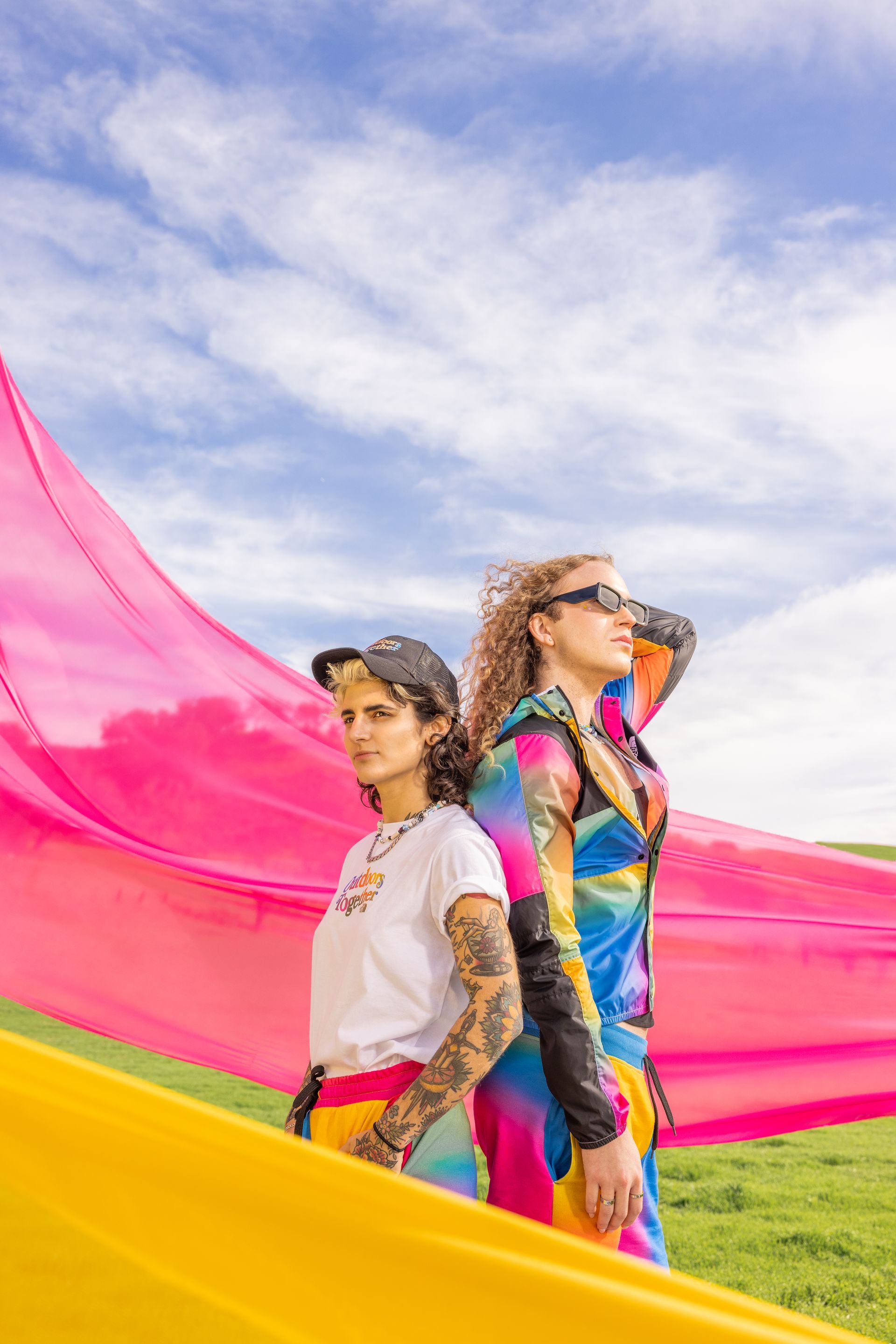 Two women are standing next to each other in a field holding a colorful flag for a NorthFace photo shoot.